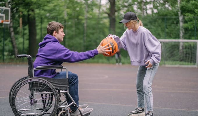 A young man in a wheelchair playing basketball with a friend at a local court