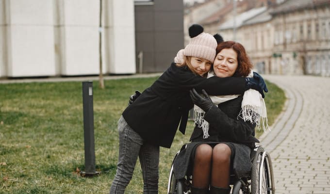 A young girl joyfully hugging a woman in a wheelchair outdoors